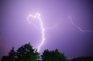 A purple sky with lightning and trees in the foreground.